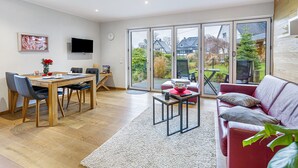 A modern living room with a dining area, a red sofa, and a TV mounted on the wall. - Holiday Apartment 'Amsel A, 50 sqm' with Mountain View, Private Terrace and Wi-Fi (Lennestadt- Saalhausen)