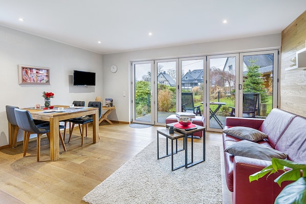 Un salon moderne comprenant un coin repas, un canapé rouge et un téléviseur fixé au mur.