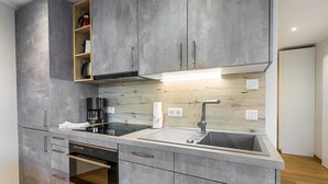 A modern kitchen with grey cabinetry, a built-in oven, a coffee maker, and a sink.