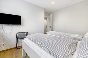 A bedroom with two beds, a TV mounted on the wall, and a chair. - Apartment 'Buchfink B, 50 sqm' with Mountain View, Private Terrace and Wi-Fi (Lennestadt- Saalhausen)