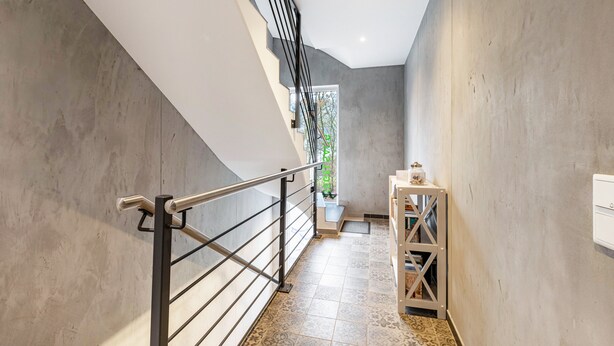 A staircase with a metal railing, a small table with a plant, and a white wall with a window.