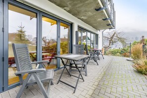 An outdoor patio with tables and chairs, a brick pathway, and a view through large glass doors. - Apartment 'Buchfink B, 50 sqm' with Mountain View, Private Terrace and Wi-Fi (Lennestadt- Saalhausen)