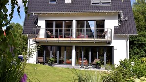 A modern two-story house with a balcony, large windows, and a well-maintained garden.