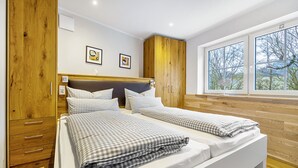 A double bed with checkered bedding, wooden wardrobe, and a window with a view.