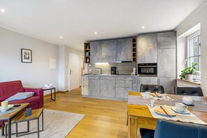 A modern kitchen with grey cabinets, a dining area with a table set for two, and a red sofa in the living area.