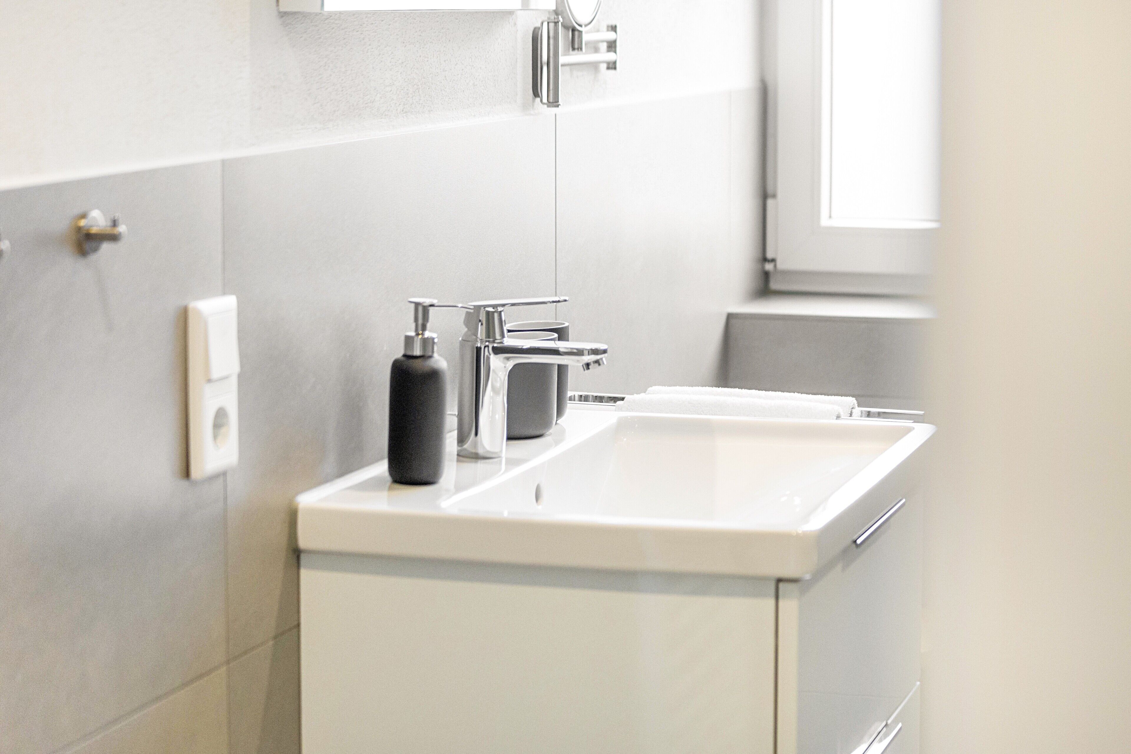 Een badkamer met een wit wastafelmeubel, een spiegel en een zeepdispenser.
