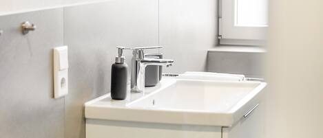 Een badkamer met een wit wastafelmeubel, een spiegel en een zeepdispenser.