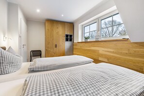 A bedroom with two beds, a wooden wardrobe, a window with a view, and a small table with a plant.