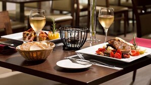 A dining table set with a basket of bread, a plate of roasted vegetables, and two glasses of white wine. - CZECH INN Hotel Ferenc (Budapest)