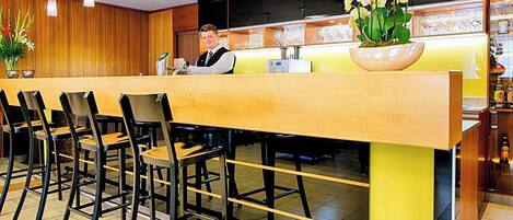 A hotel reception area with a long counter, several chairs, and a large vase of flowers.