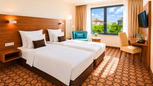 A hotel room with two beds, a desk, a chair, a TV, and a window with a view of buildings and trees. - CZECH INN Hotel Ferenc (Budapest)