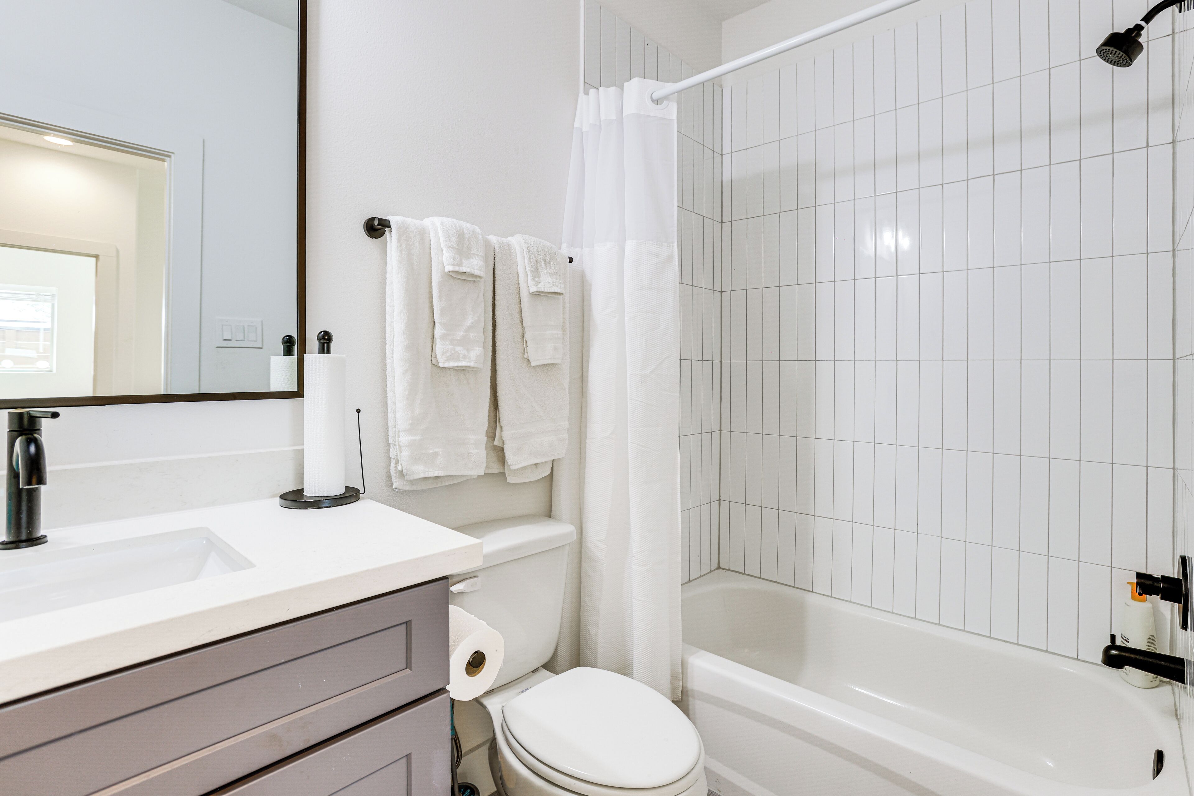 Une salle de bain avec un lavabo, des toilettes et une baignoire, tous de couleur blanche. Des serviettes sont accrochées au mur et il y a un rideau de douche.
