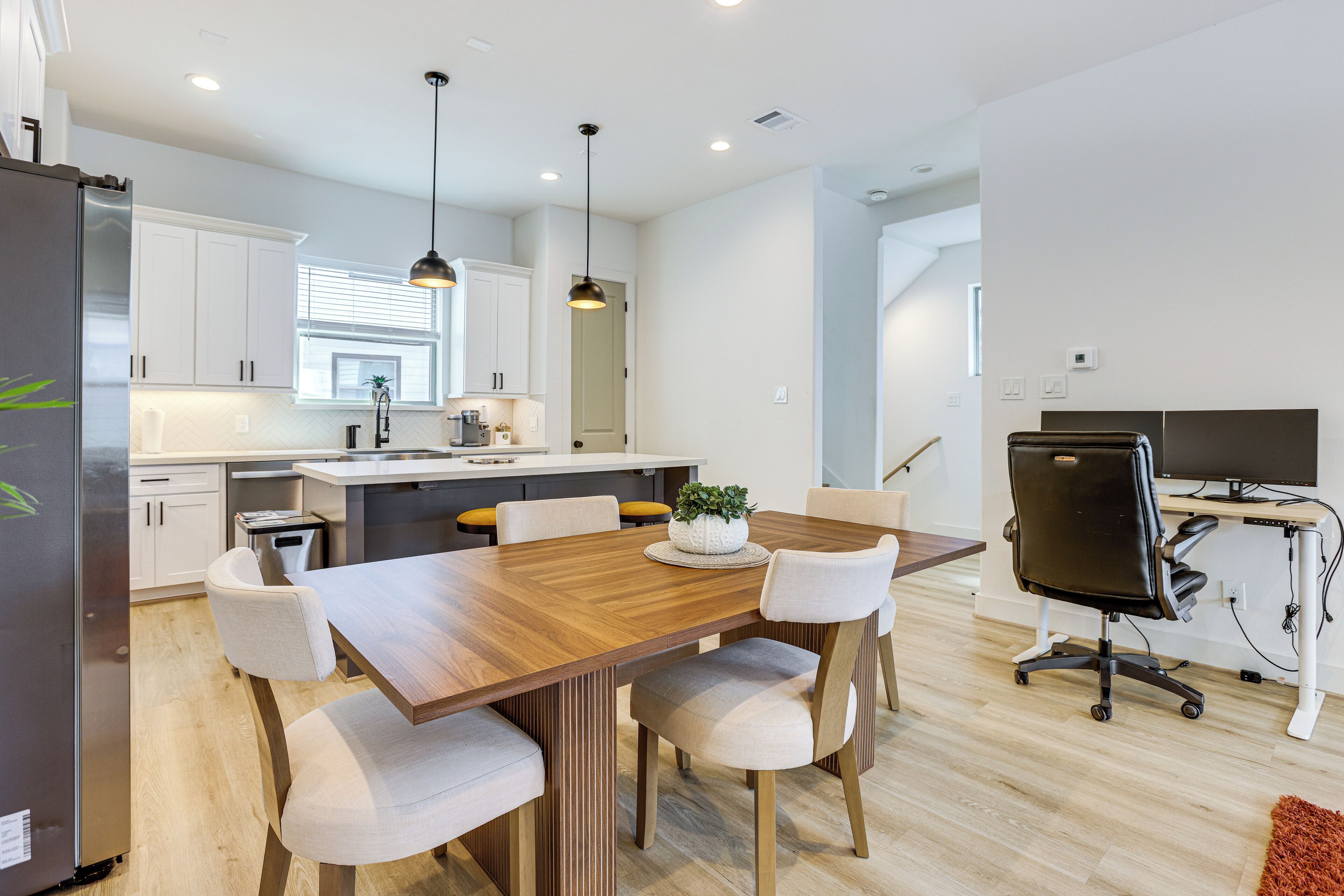 A modern kitchen with white cabinets, a wooden dining table, and a black office chair.