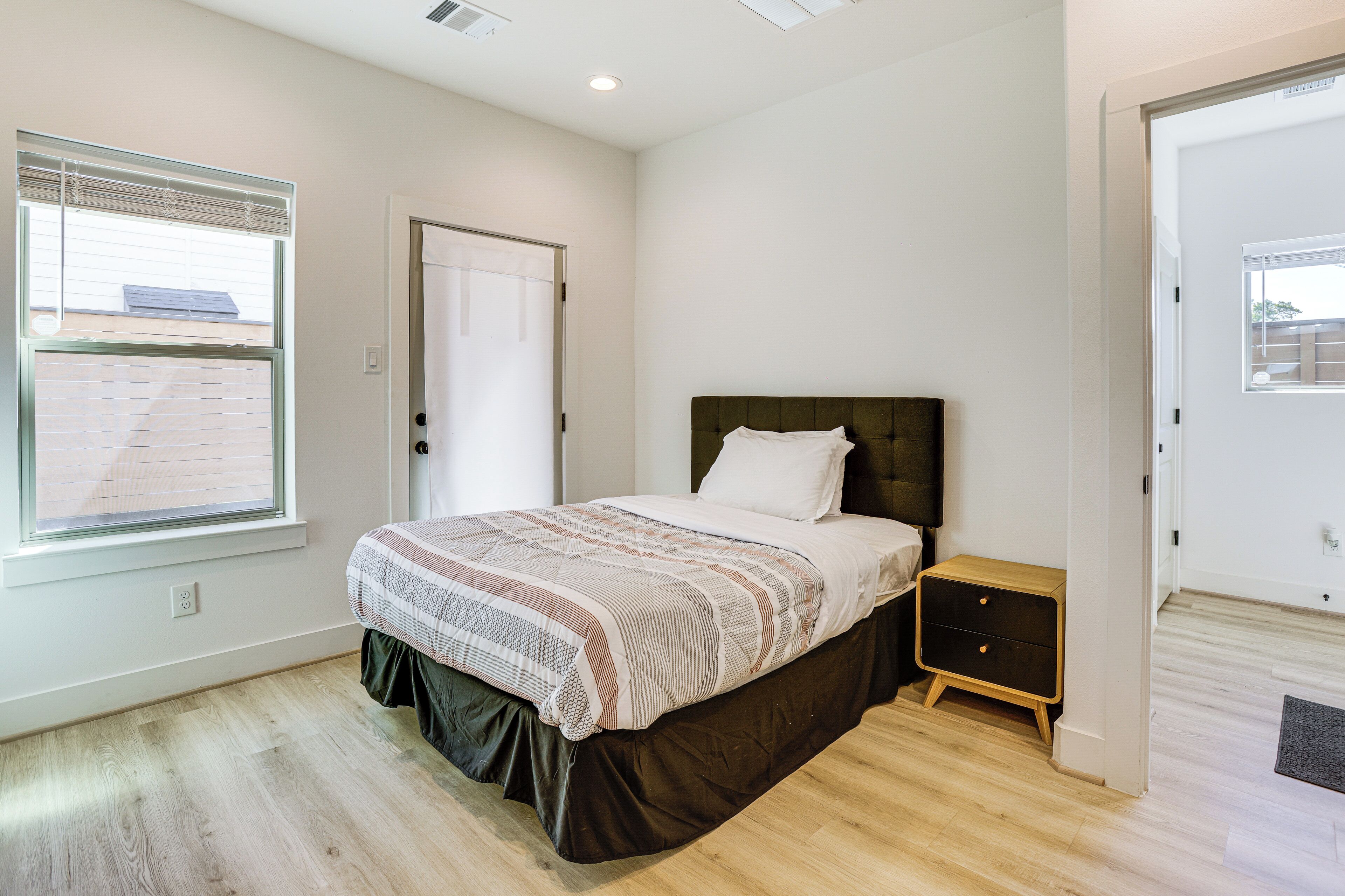 A bedroom with a bed, a nightstand, a window, and a door.