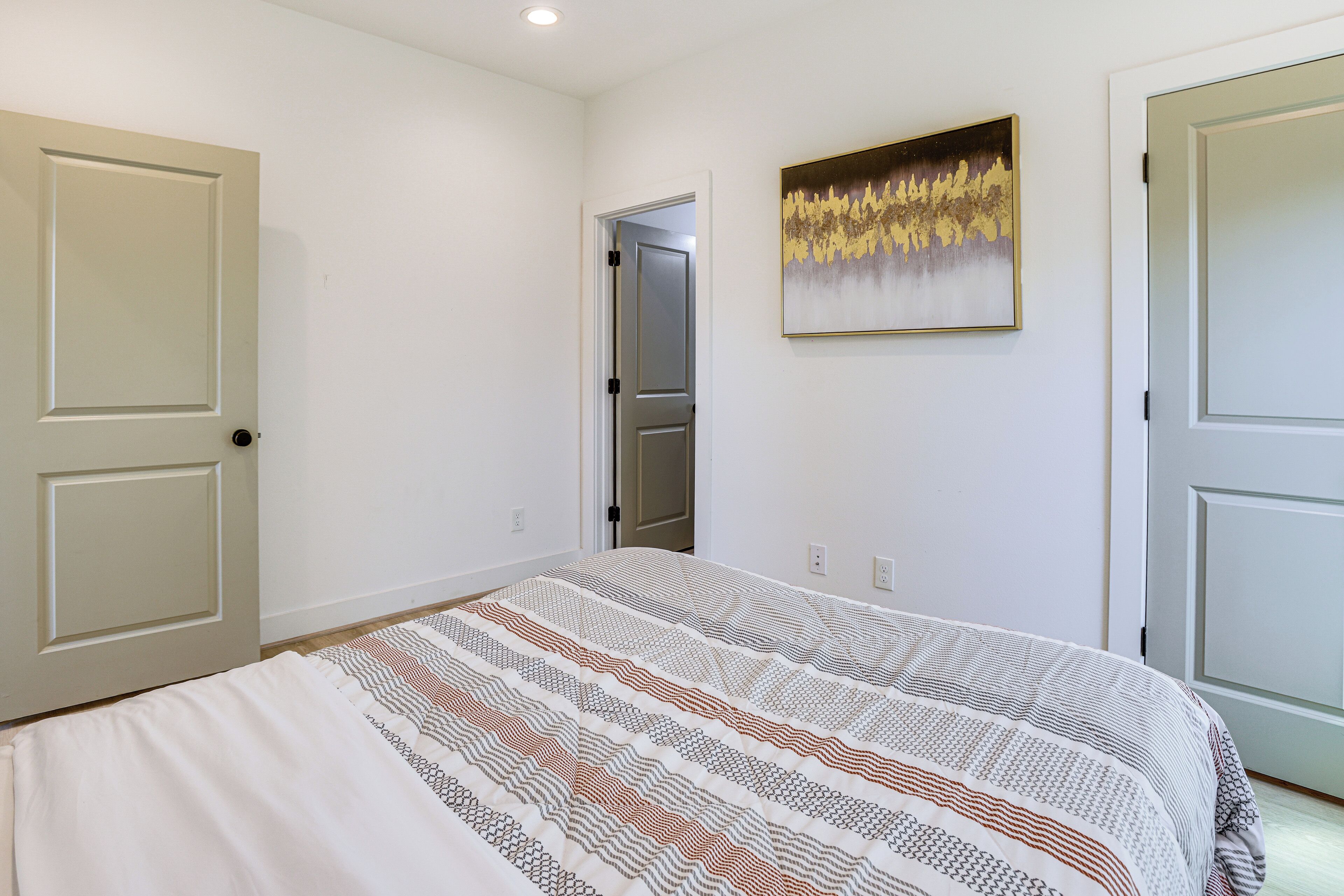 Un dormitorio con una cama, una puerta y un cuadro en la pared.