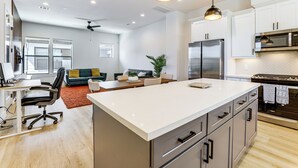 Eine moderne Küche mit Edelstahlgeräten, einer großen Kochinsel und einem Essbereich mit einer Couch und Couchtisch.