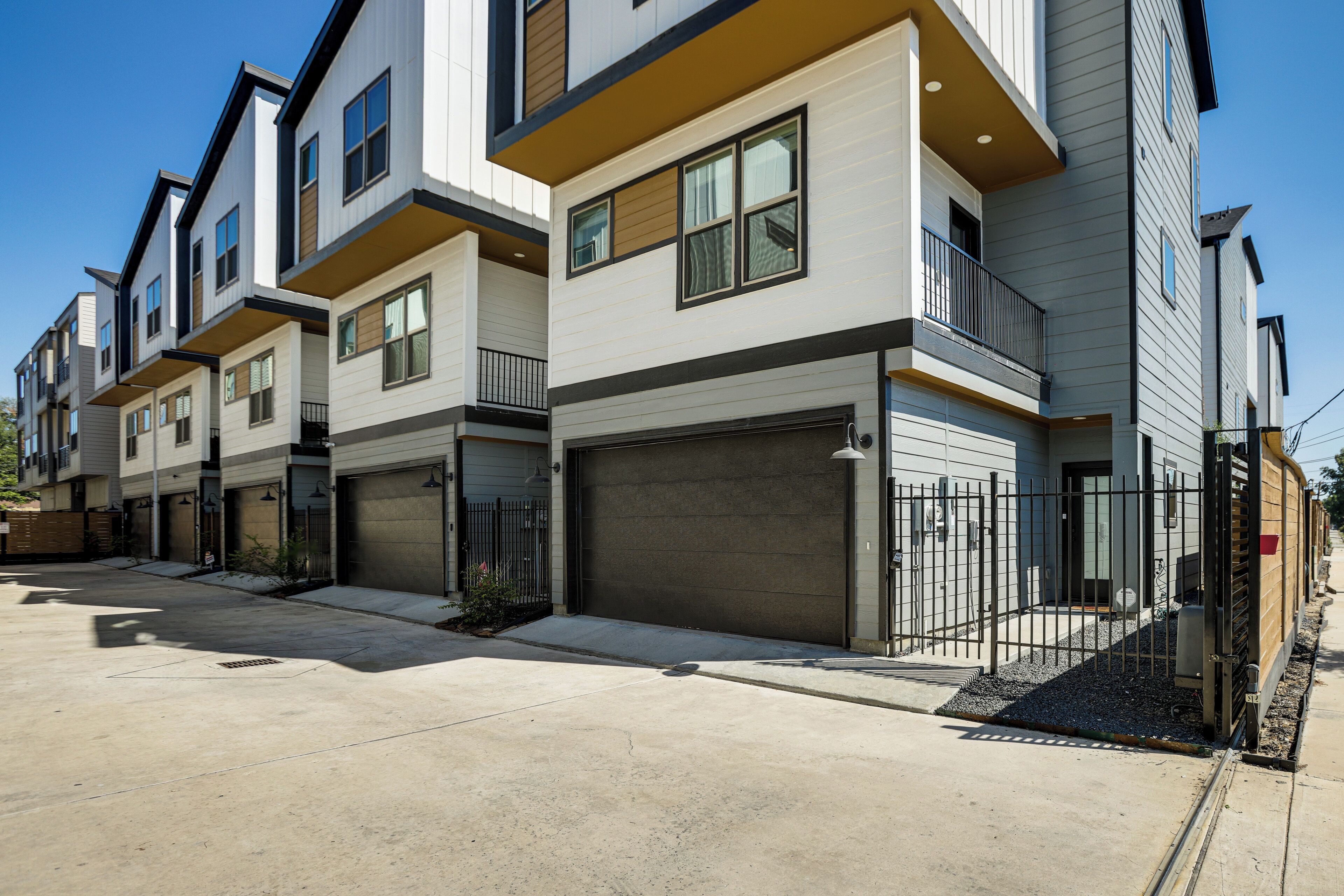 Une rangée de maisons de ville modernes, dotées de garages attenants, d’une allée en béton et d’une entrée fermée par un portail.