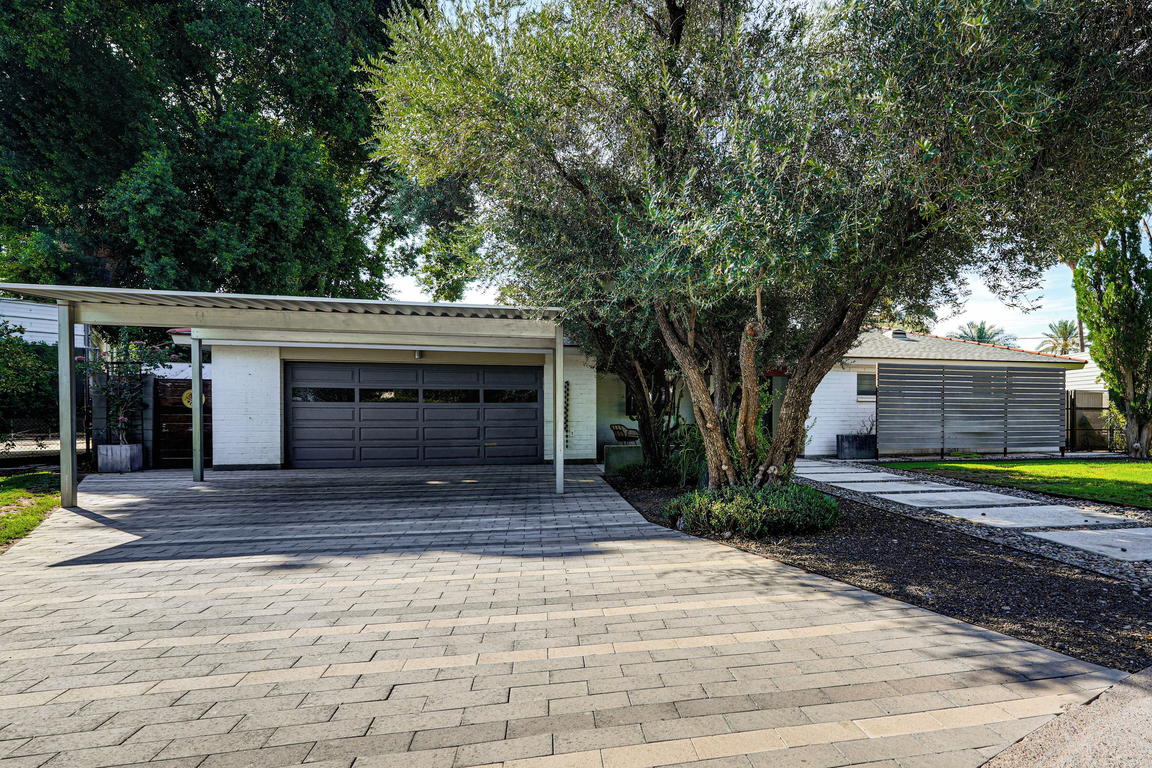 A residential garage with a covered driveway and a tree in the foreground.