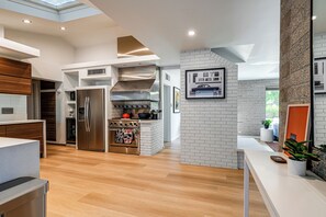Une cuisine moderne dotée d’un réfrigérateur, d’un four et d’un micro-ondes en acier inoxydable, de meubles de rangement en bois et d’un mur d’accent en briques.