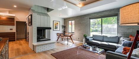 A modern living room with a fireplace, a sofa, a dining area, and a large window.