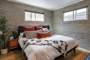 A bedroom with a brick-patterned wall, a bed with multiple pillows, a nightstand with a green vase, and a potted plant. - 1 Mi to Dtwn & Mill Avenue! Home w/ Outdoor Oasis (Tempe)