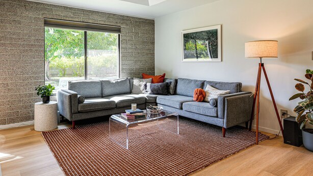 Ein modernes Wohnzimmer mit einem grauen Sofa, einem Couchtisch und einem Teppich mit Muster.