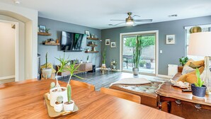 A spacious living room with a wooden dining table, a leather sofa, and a TV mounted on the wall. - Pool Access! Suburban Home 11 Mi to Dtwn Gilbert (Gilbert)