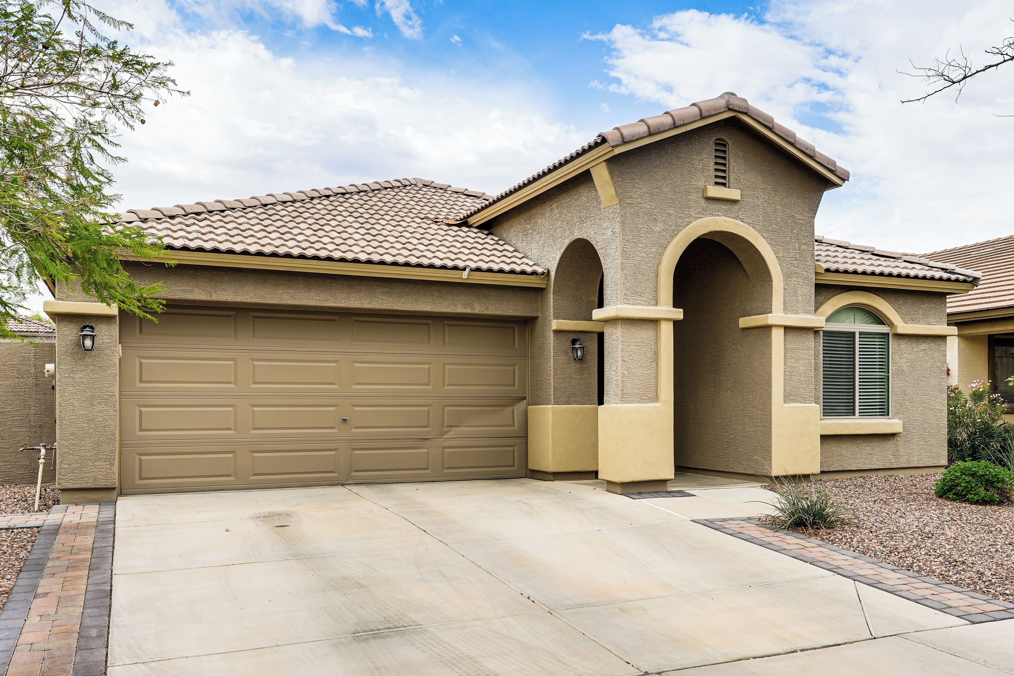 A residential house with a beige garage door, a small arched entrance, and a tiled roof.