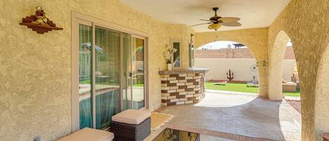 A covered patio with wicker furniture, a glass door leading outside, and a decorative wall.