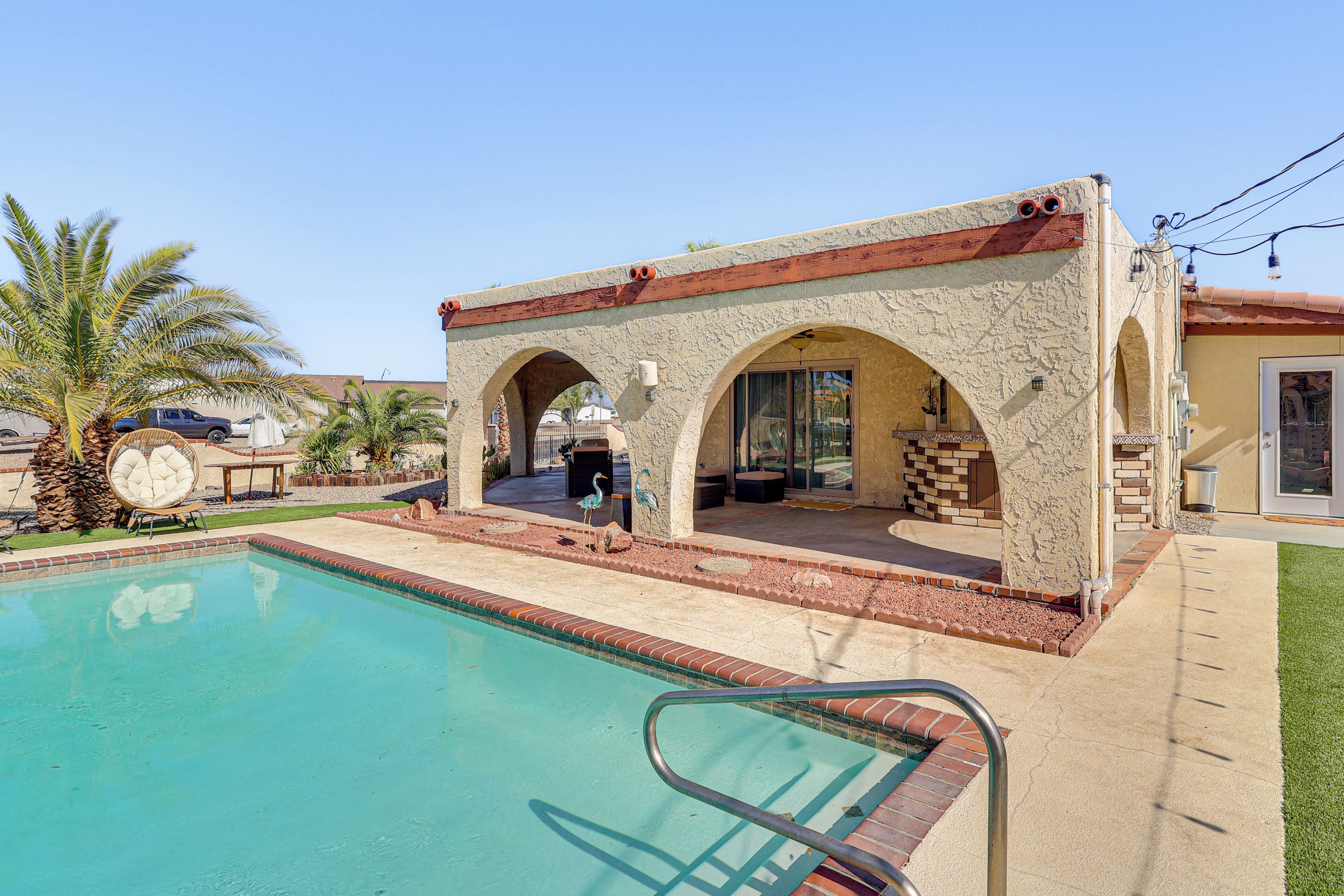 A pool area with a stone structure, palm trees, and a clear blue sky.