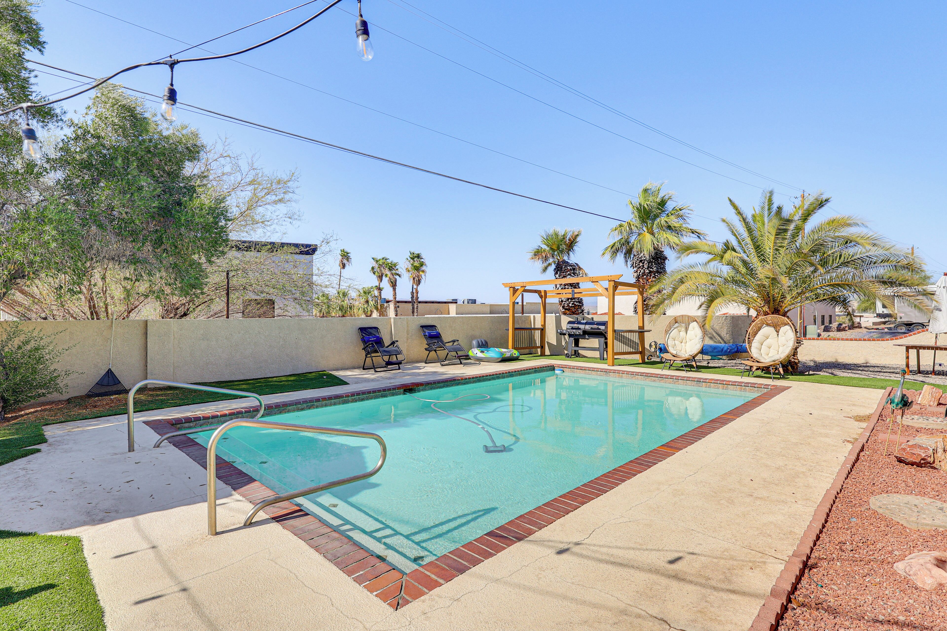 Une piscine rectangulaire bordée de briques, entourée d’une terrasse en béton. On y trouve des chaises longues et une pergola avec une table et des chaises.