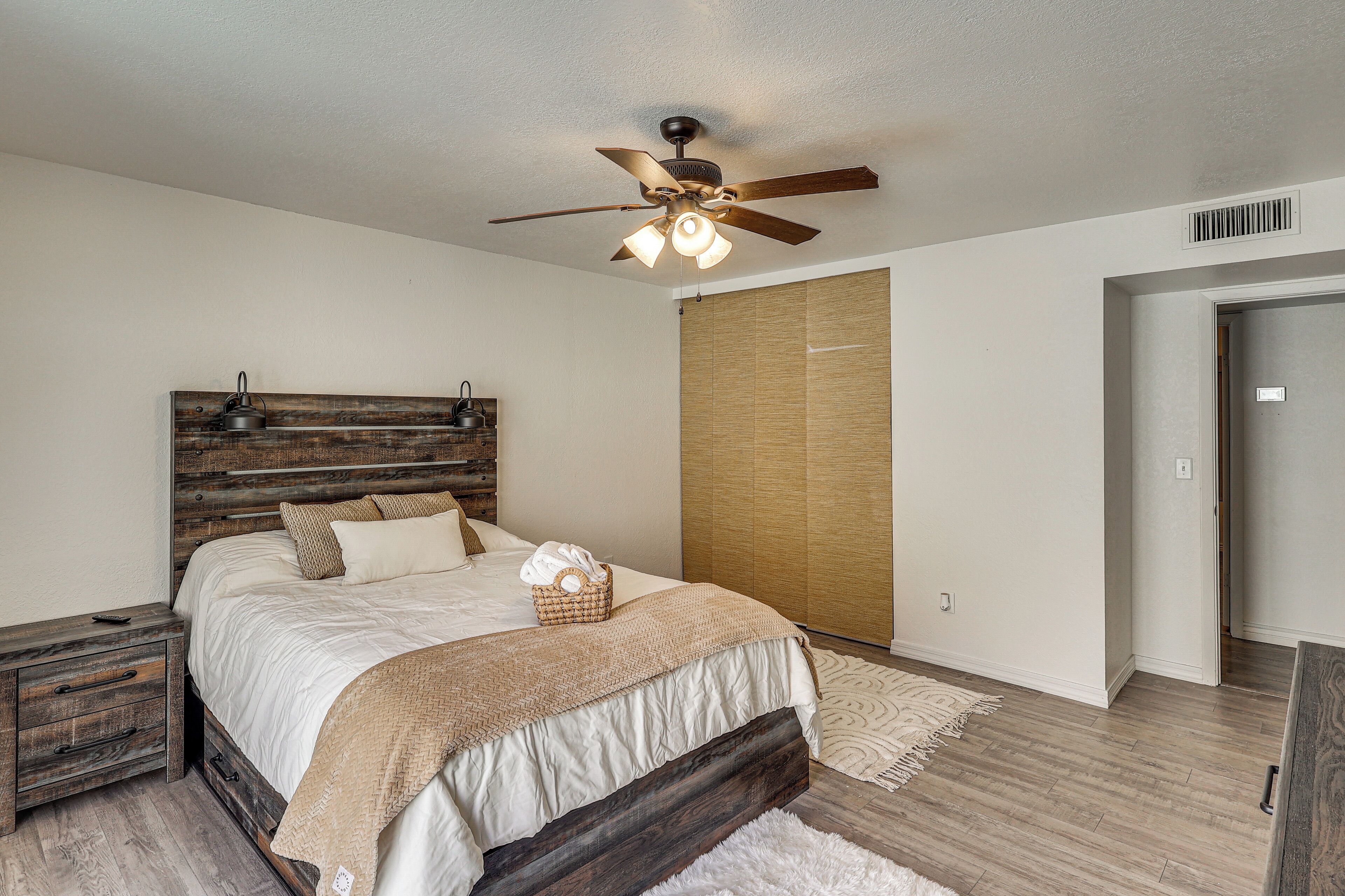 A bedroom with a wooden headboard, a bed with white bedding, a ceiling fan, and a wooden wardrobe.