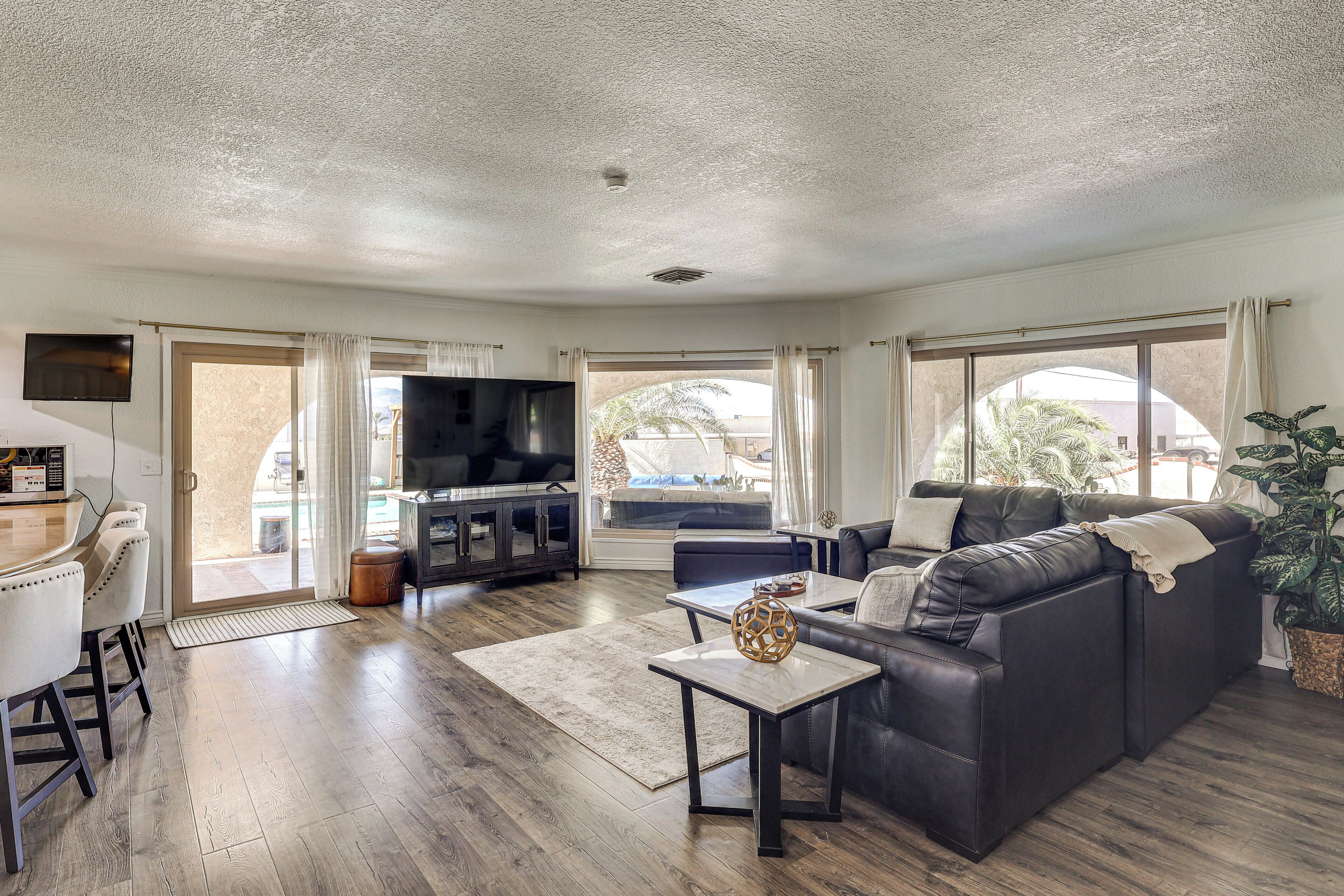 A spacious living room with a large black leather sofa, a wooden coffee table, and a flat-screen TV mounted on the wall.