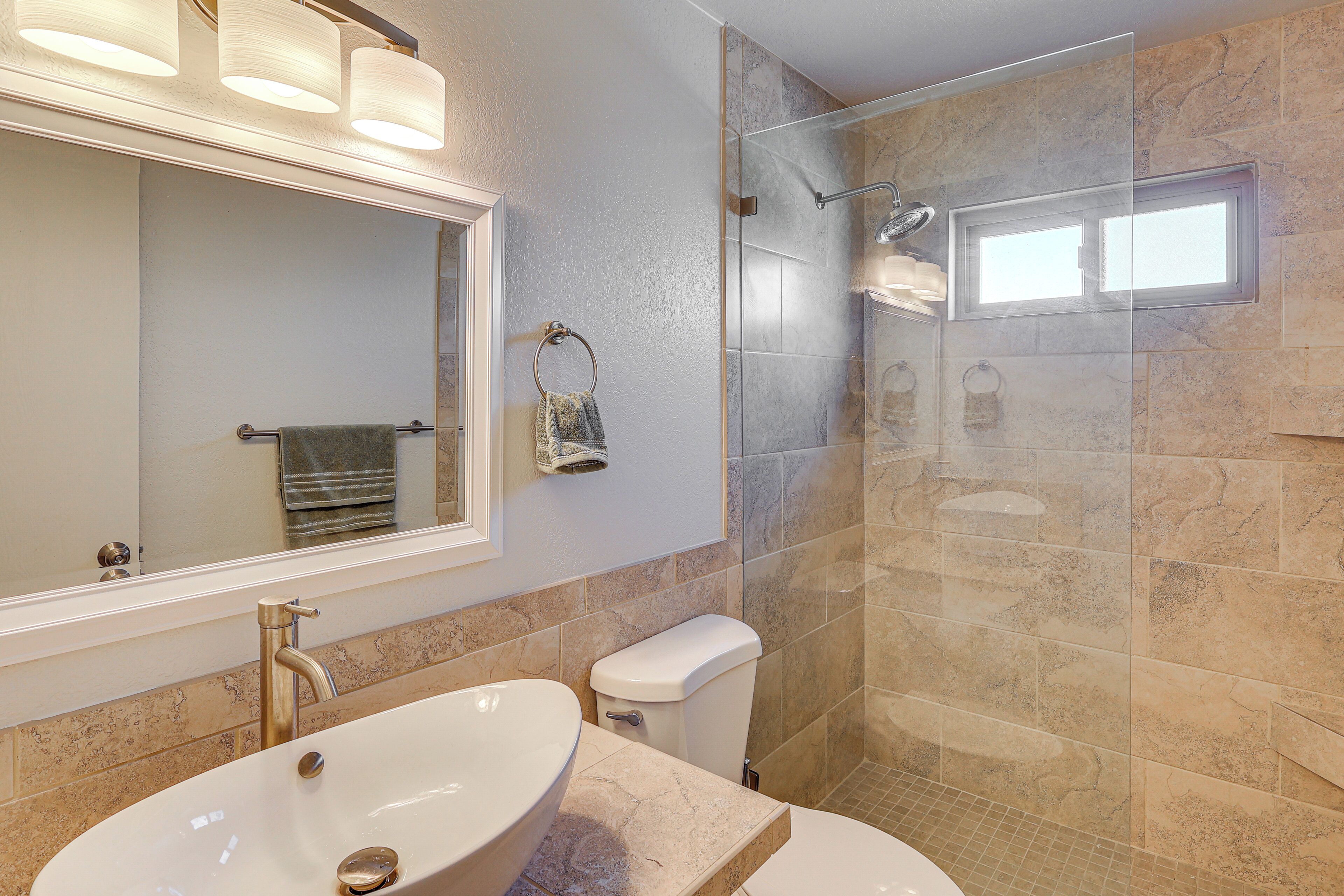 Une salle de bain dotée d’un grand lavabo ovale, d’un miroir, d’un porte-serviettes et d’une cabine de douche en verre.