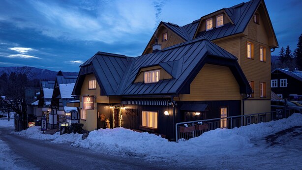 A large, multi-story building with a steeply pitched roof, multiple windows, and a snow-covered ground. - Pension U Komárků (Špindlerův Mlýn)