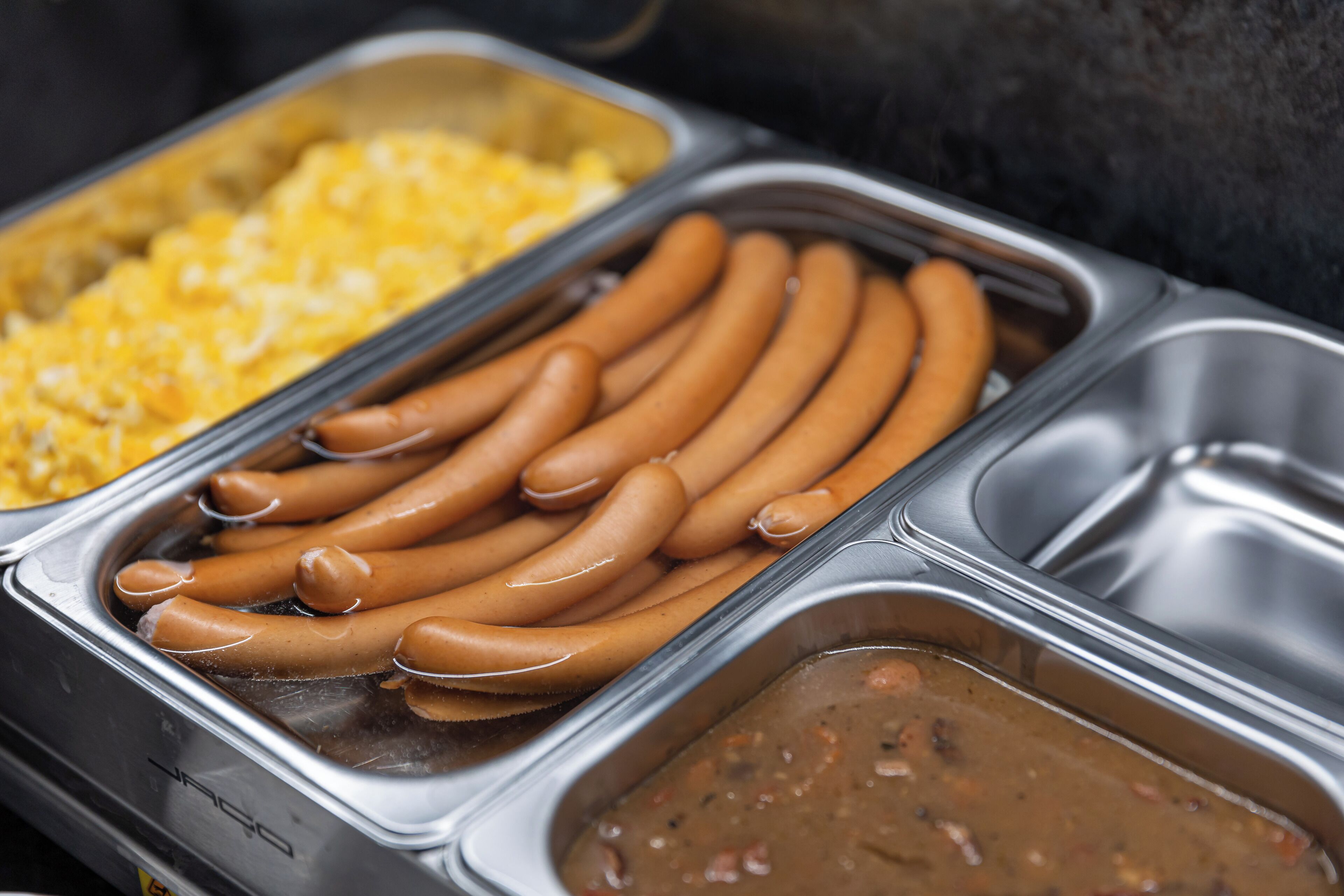 A buffet with hot dogs, macaroni, and a brown sauce.