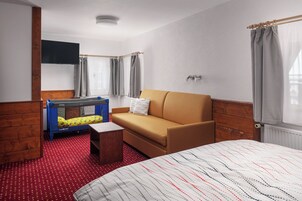 Habitación de hotel con cama, sofá, una mesita, literas y ventana con cortinas.