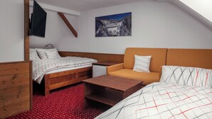 A compact room with a bed, a sofa, a small table, a TV, and a painting on the wall. - Pension U Komárků (Špindlerův Mlýn)
