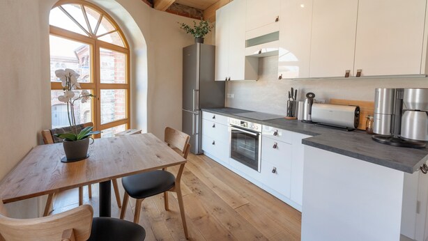 Una cocina moderna con armarios blancos, una mesa de comedor de madera y un ventanal con arco.
