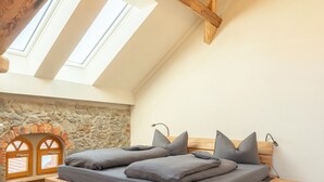 Un dormitorio tipo loft con cama de madera, tragaluces, chimenea de piedra y vigas de madera a la vista.