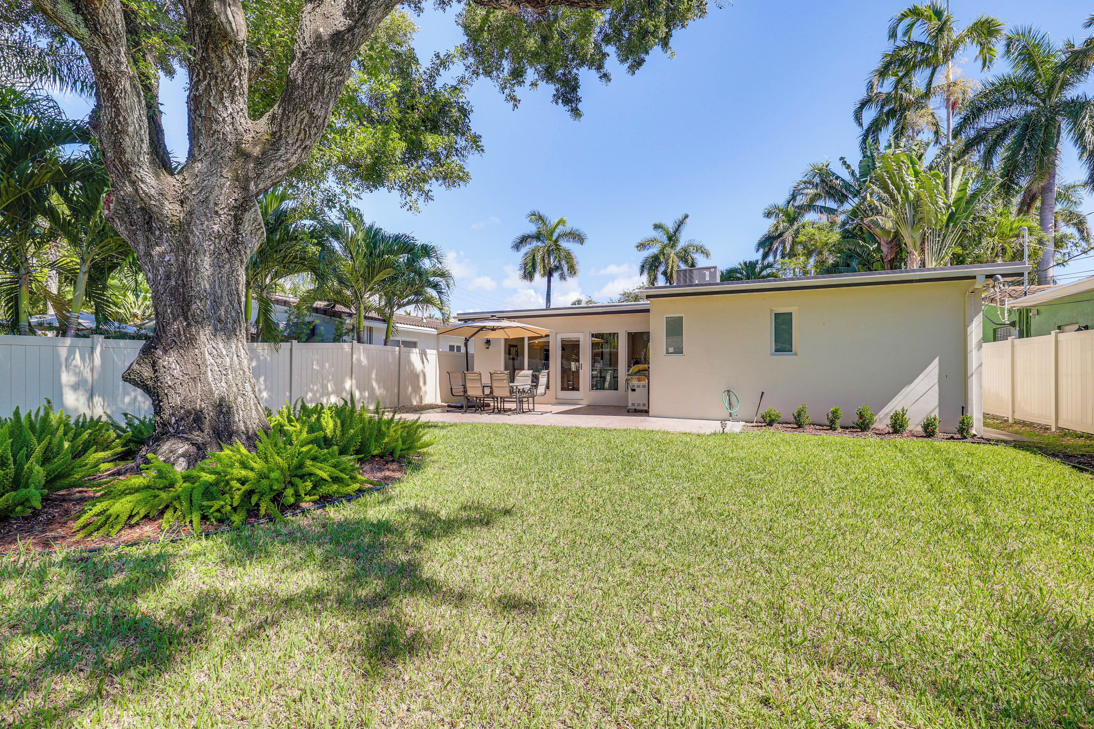 A residential property with a well-maintained lawn, a large tree, and a patio area with outdoor furniture.
