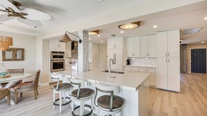 A modern kitchen with a central island, bar stools, and a dining area with wicker chairs. - Spacious Yard, Near Golf: Modern Home in Hollywood (Hollywood)