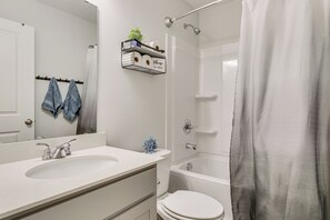 Ein Badezimmer mit weißem Waschbecken, Toilette, Dusche und Handtuchhalter mit Handtüchern.