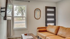 A room with a brown leather sofa, a wooden coffee table, a mirror on the wall, and a window with curtains. - Near Historic Georgetown Square! Updated Home (Georgetown)