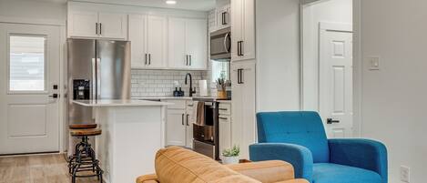 A modern kitchen with white cabinets, stainless steel appliances, and a blue chair.
