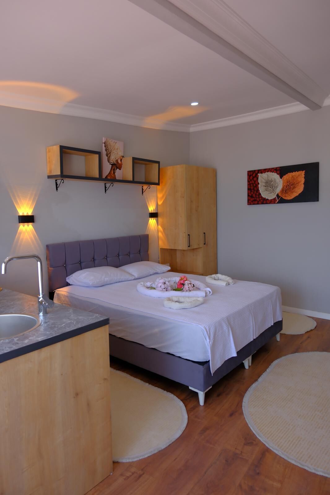 A bedroom with a bed, a wooden wardrobe, a bedside table with a lamp, and a wall-mounted shelf with decorative items.