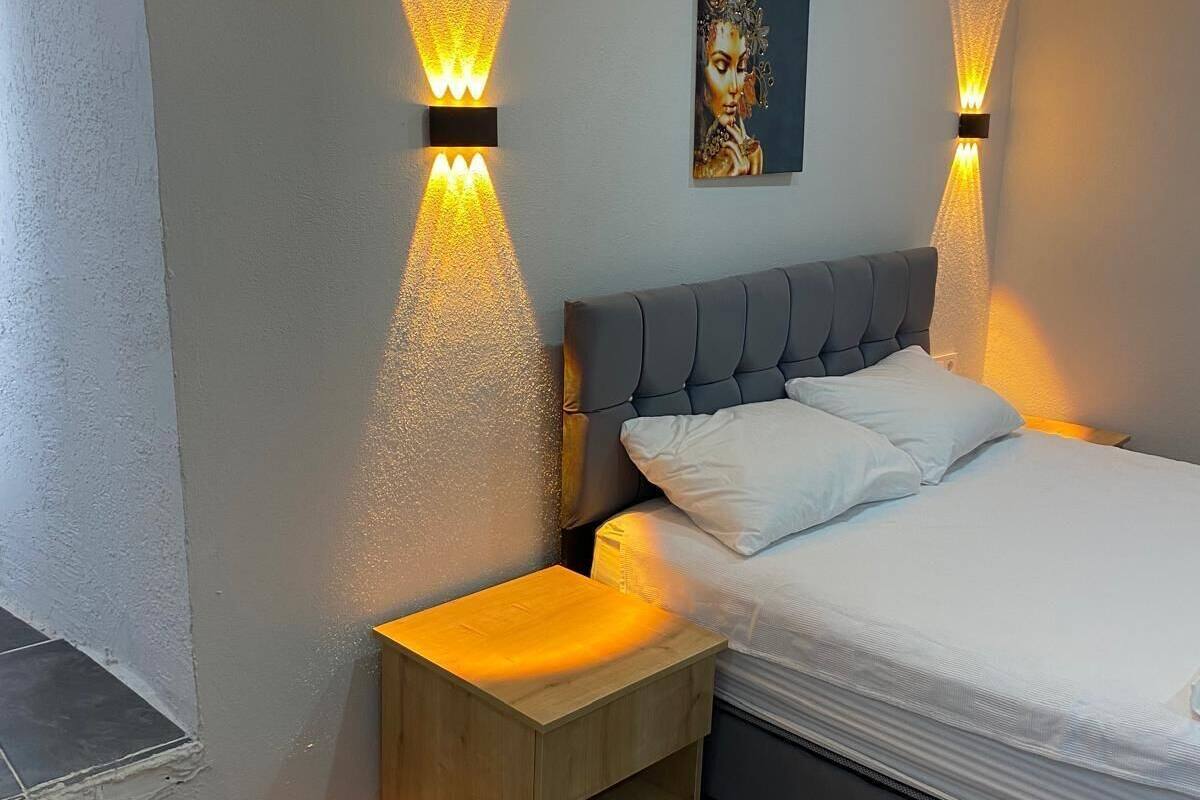 A modern bedroom with a grey upholstered bed, white pillows, and a small wooden nightstand.