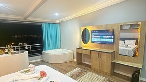 A modern hotel room with a large bed, a desk, a TV, and a balcony with a city view. - FETHİYE OLD TOWN SUİTES (Fethiye)