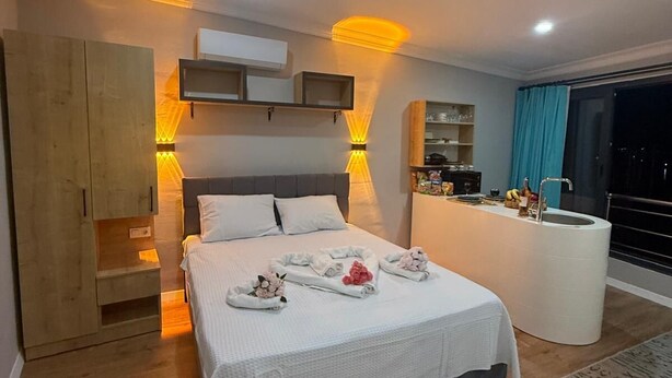 A modern bedroom with a large bed, bedside tables, a vanity with a mirror, and a view of the outside through a large window. - FETHİYE OLD TOWN SUİTES (Fethiye)