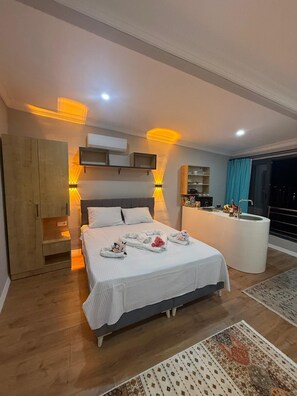 Um quarto moderno com uma cama grande, mesas de cabeceira, uma cômoda com espelho e vista para o exterior por uma grande janela.